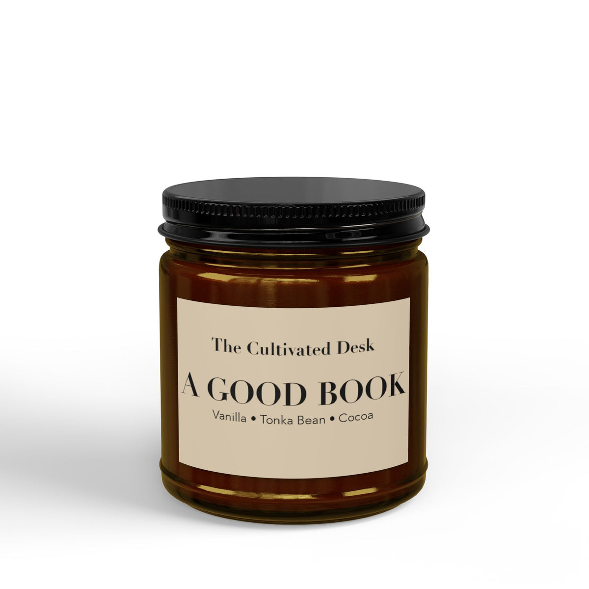 Cozy scented candle in a 4oz amber glass jar featuring a minimalist cream label with the text "The Cultivated Desk," "A GOOD BOOK," and scent notes "Vanilla • Tonka Bean • Cocoa" in black serif typography, sealed with a ribbed black metal lid. Scented candle titled 'A Good Book', available in 9oz and 4oz sizes.