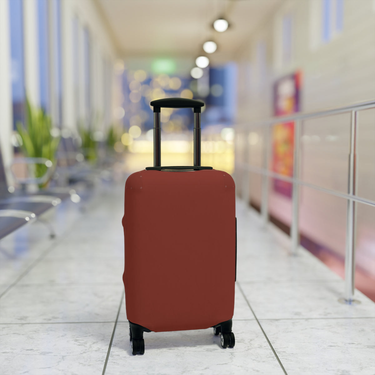 A terracotta red elastic luggage cover fitted on a rolling suitcase, standing upright in a brightly lit, blurred airport terminal corridor.