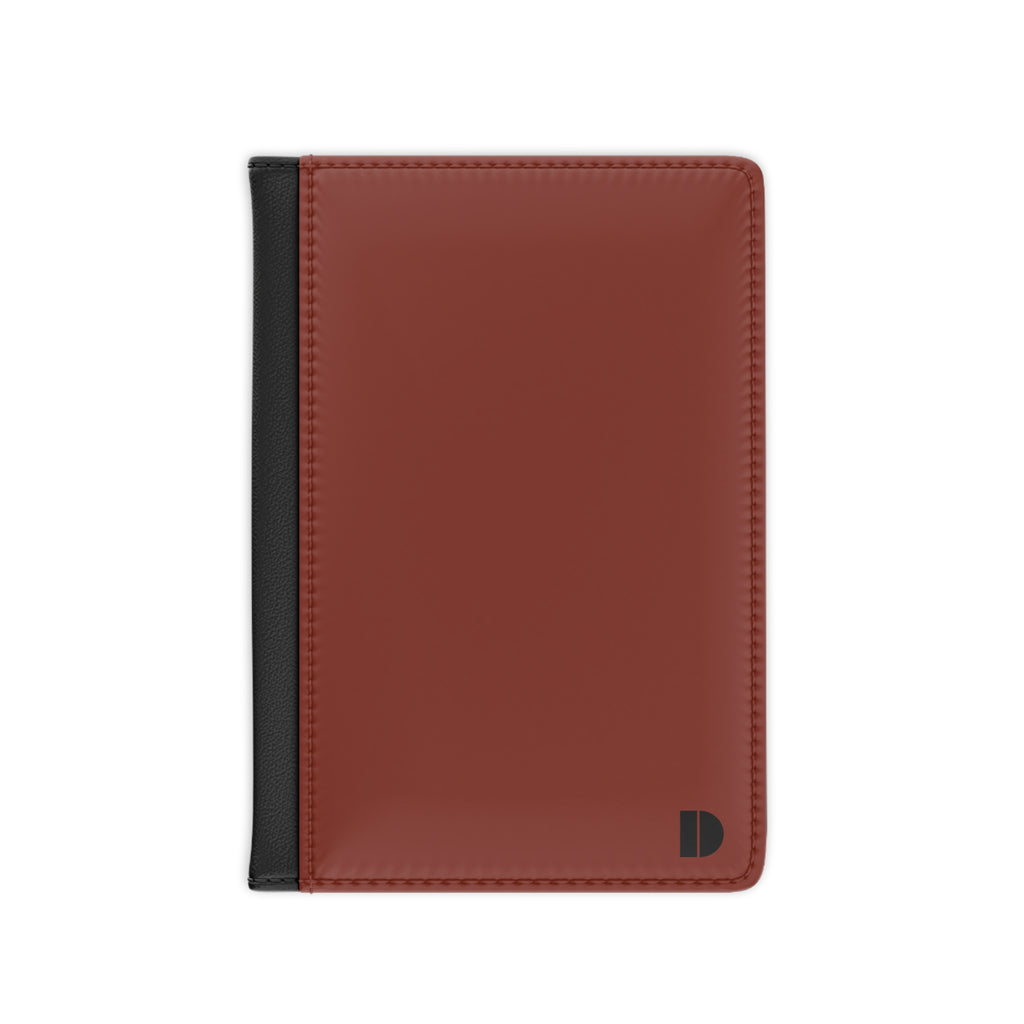 A minimalist faux leather passport cover in a warm reddish-brown color with a contrasting black spine strip and a small black monogram logo in the bottom right corner, shown on a plain white background.
