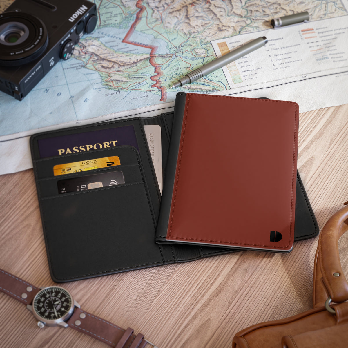 A minimalist faux leather passport holder wallet shown open and closed on a wooden tabletop with travel props including a map, camera, pen, cards, watch, and bag.