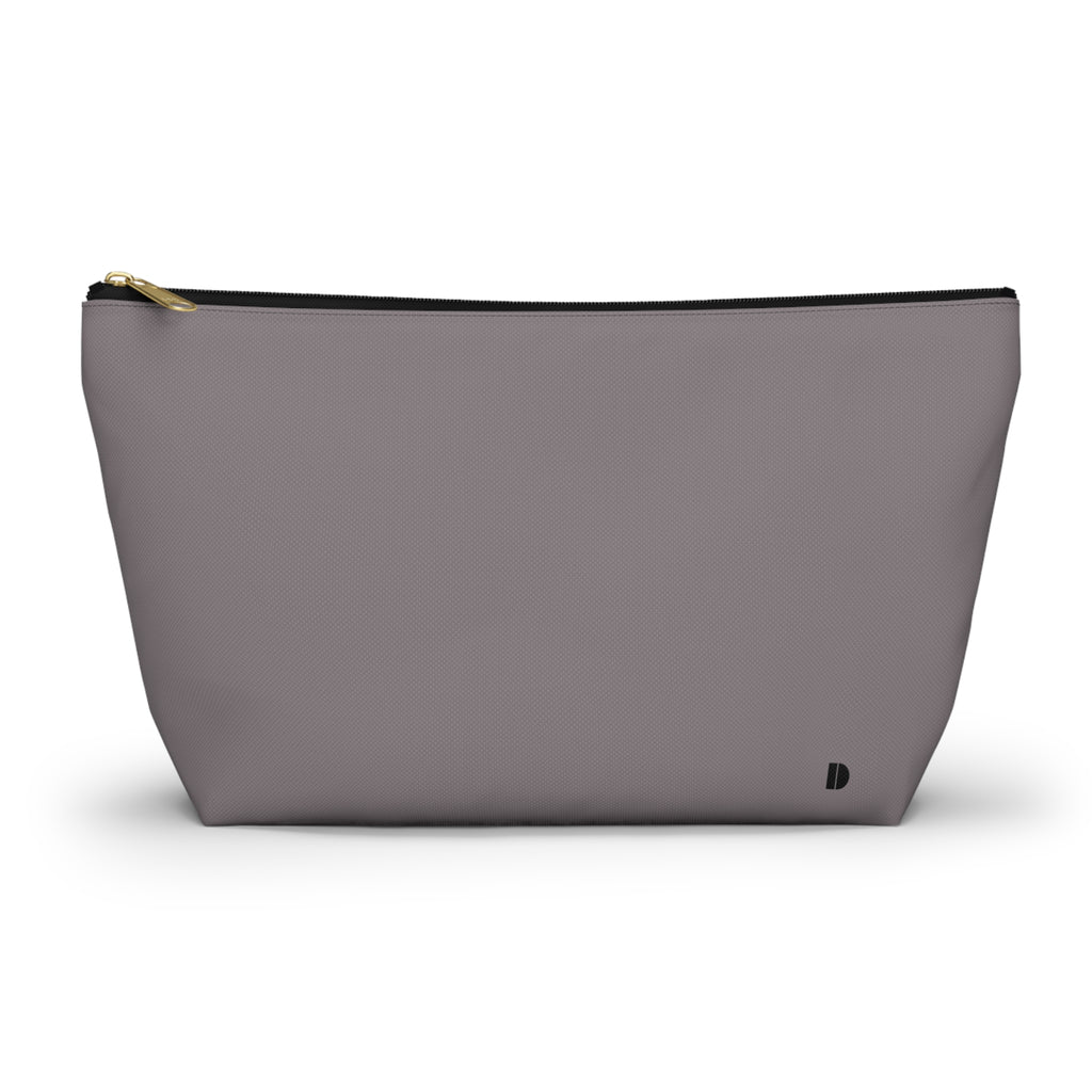 A minimalist makeup pouch in a muted gray  color, featuring a gold zipper pull and a small black monogram logo on the bottom right, set against a plain white background.
