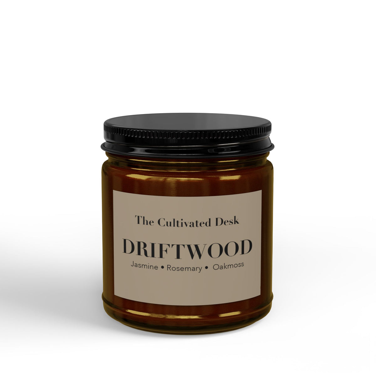 Woody scented candle in a 4oz amber glass jar featuring a minimalist warm tan label with the text "The Cultivated Desk," "DRIFTWOOD," and scent notes "Jasmine • Rosemary • Oakmoss" in black serif typography, sealed with a ribbed black metal lid. Scented candle titled 'Driftwood', available in 9oz and 4oz sizes.