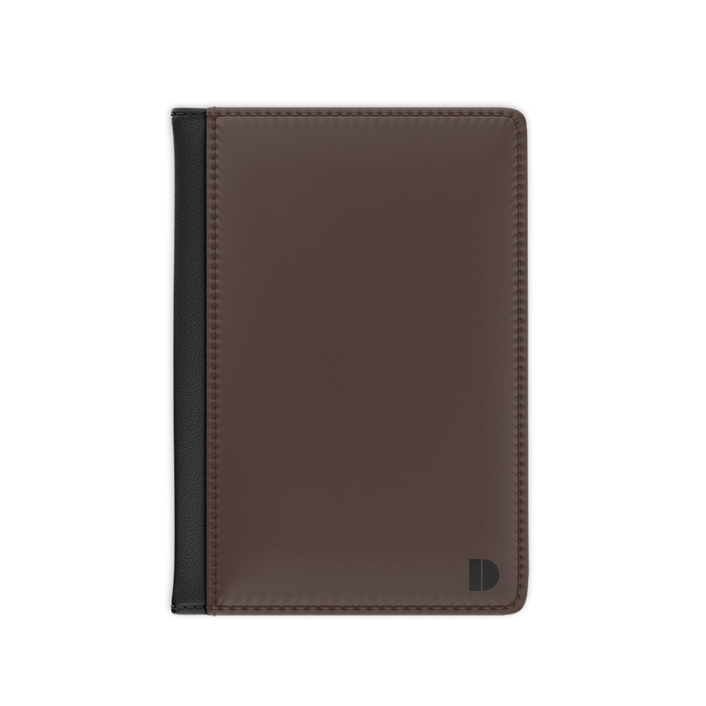 A dark brown faux leather passport cover with a black spine band and a small black monogram logo in the bottom right corner, shown on a plain white background.