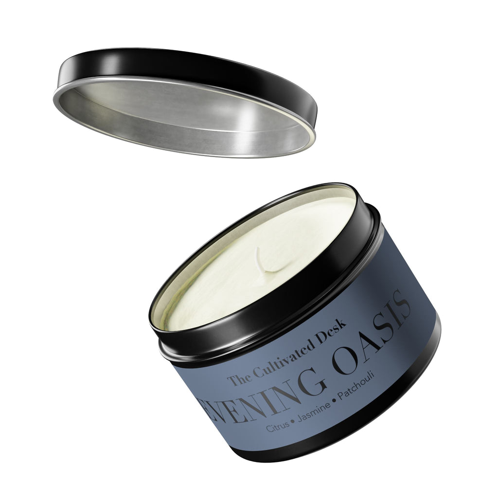 An open round metal tin candle with a black lid resting above it on a white background. The soy candle wax is visible inside, and the label reads 'The Cultivated Desk' and 'EVENING OASIS' with 'Citrus • Jasmine • Patchouli' below.