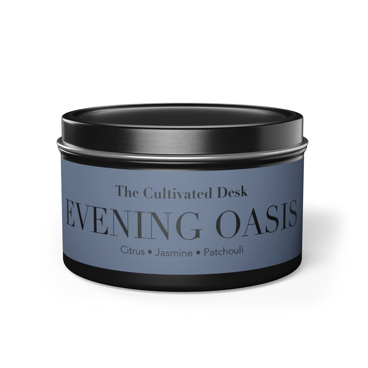 A round metal tin candle with a black lid and base, featuring a dusty blue label that reads 'The Cultivated Desk EVENING OASIS' with citrus, jasmine, and patchouli notes.
