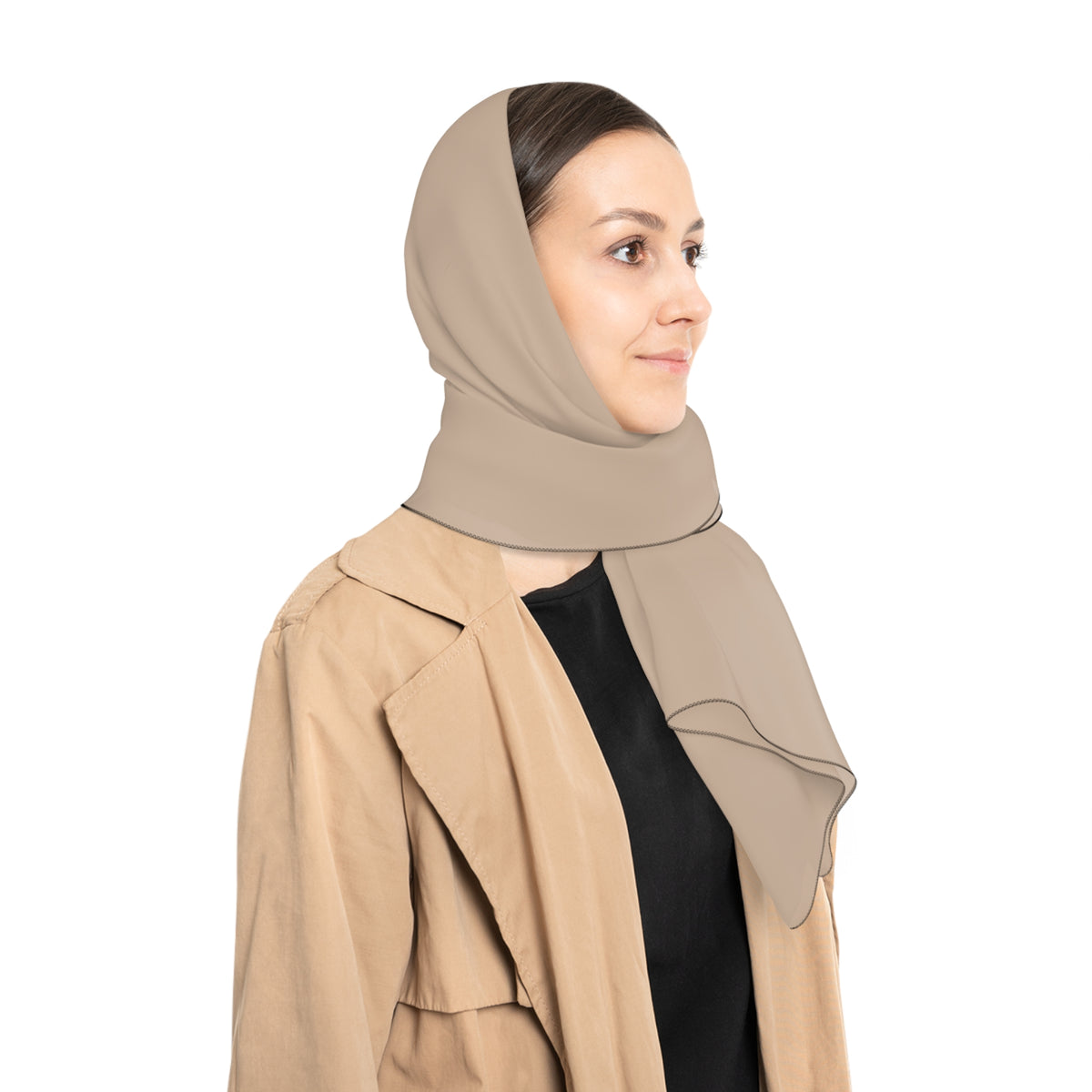 A woman shown in profile wearing a taupe-beige wrap as a head scarf and a tan trench coat over a black top, against a plain white background.