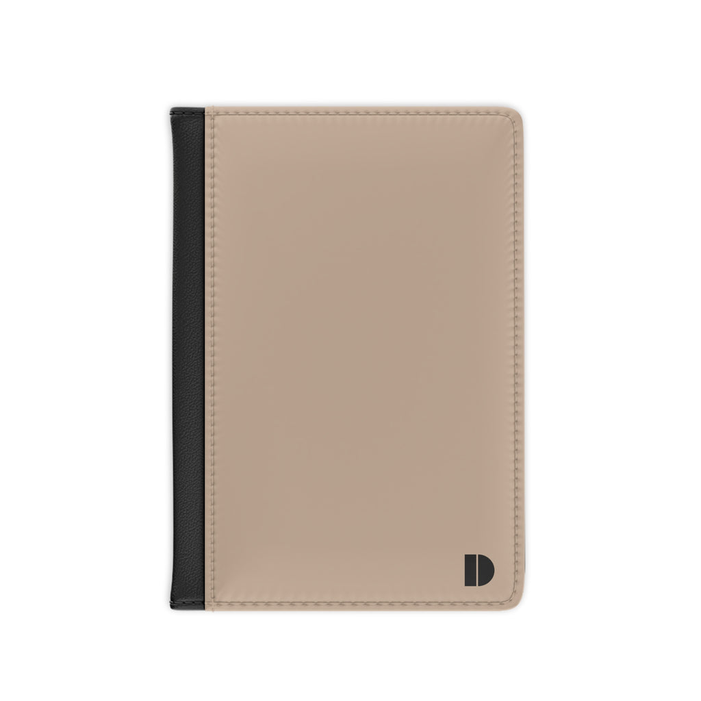 A minimalist passport cover or document holder in beige faux leather with a black spine strip and a small black monogram logo in the bottom right corner, shown on a plain white background.