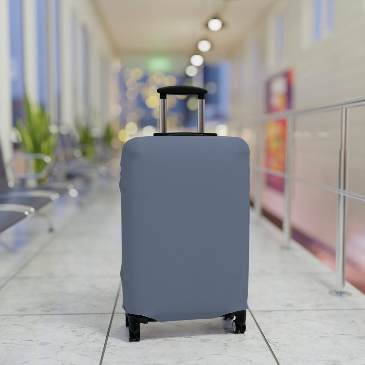 A light blue-gray fitted luggage cover on a rolling suitcase in an airport terminal corridor.