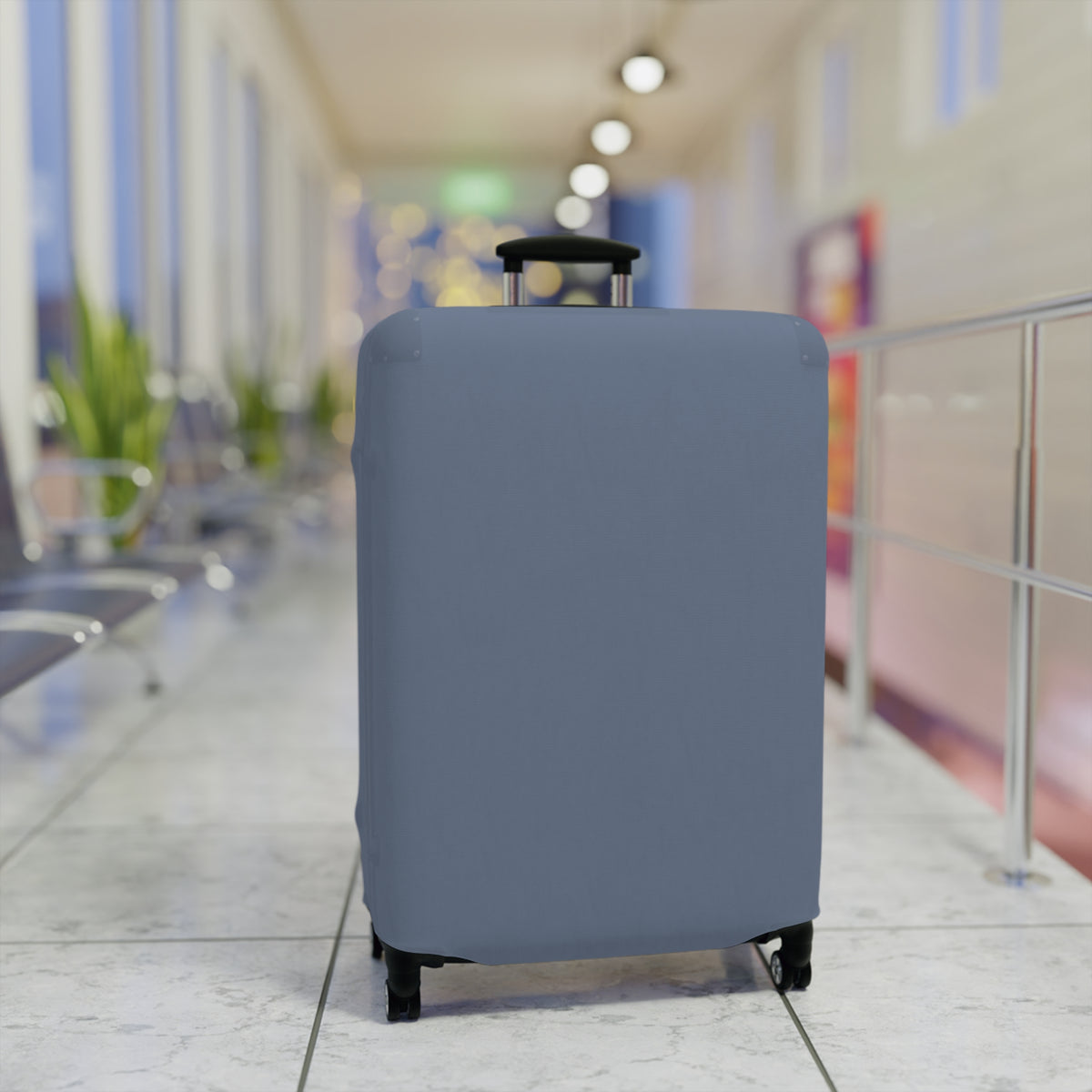 A light blue protective luggage cover fitted on a hard-shell suitcase with an extended telescoping handle and four wheels, standing upright in a brightly lit airport terminal corridor.
