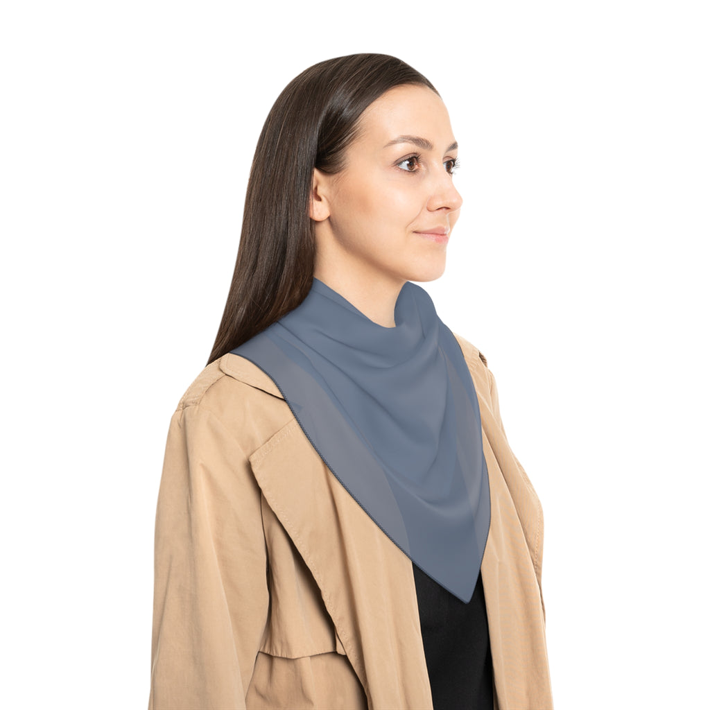 A woman shown in profile wearing a slate blue triangular neck scarf or shawl over a beige trench coat and black top, against a plain white background.