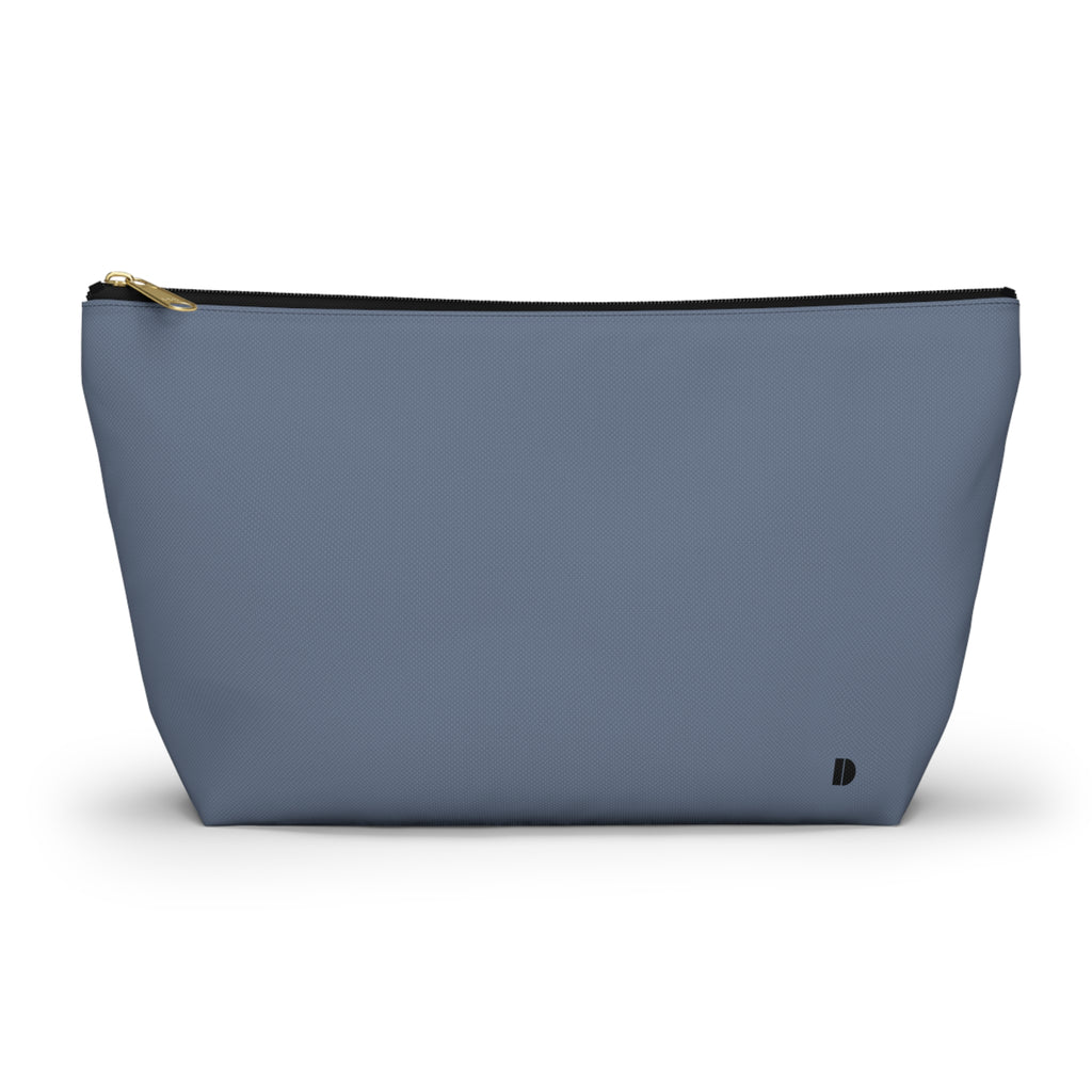A dusty blue zippered pouch with a small black monogram logo on the bottom right corner and a gold zipper pull, shown on a plain white background.