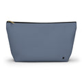 A dusty blue zippered pouch with a small black monogram logo on the bottom right corner and a gold zipper pull, shown on a plain white background.
