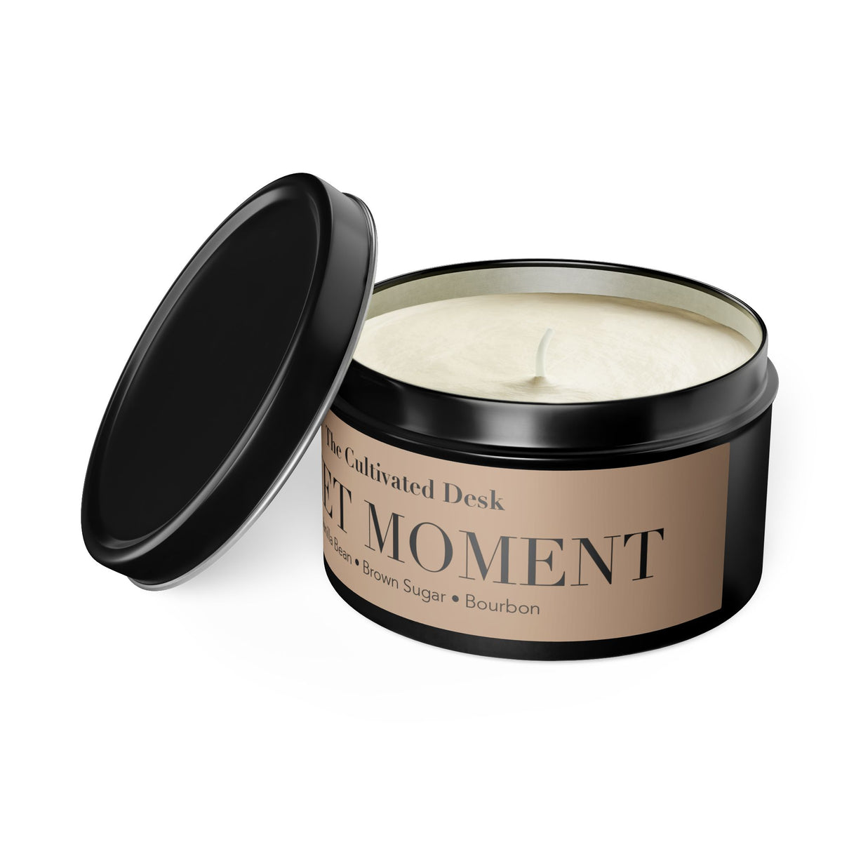 A black metal tin candle with its lid leaning against it on a white background. The soy candle wax is visible, and the label reads 'The Cultivated Desk' and 'QUIET MOMENT'.
