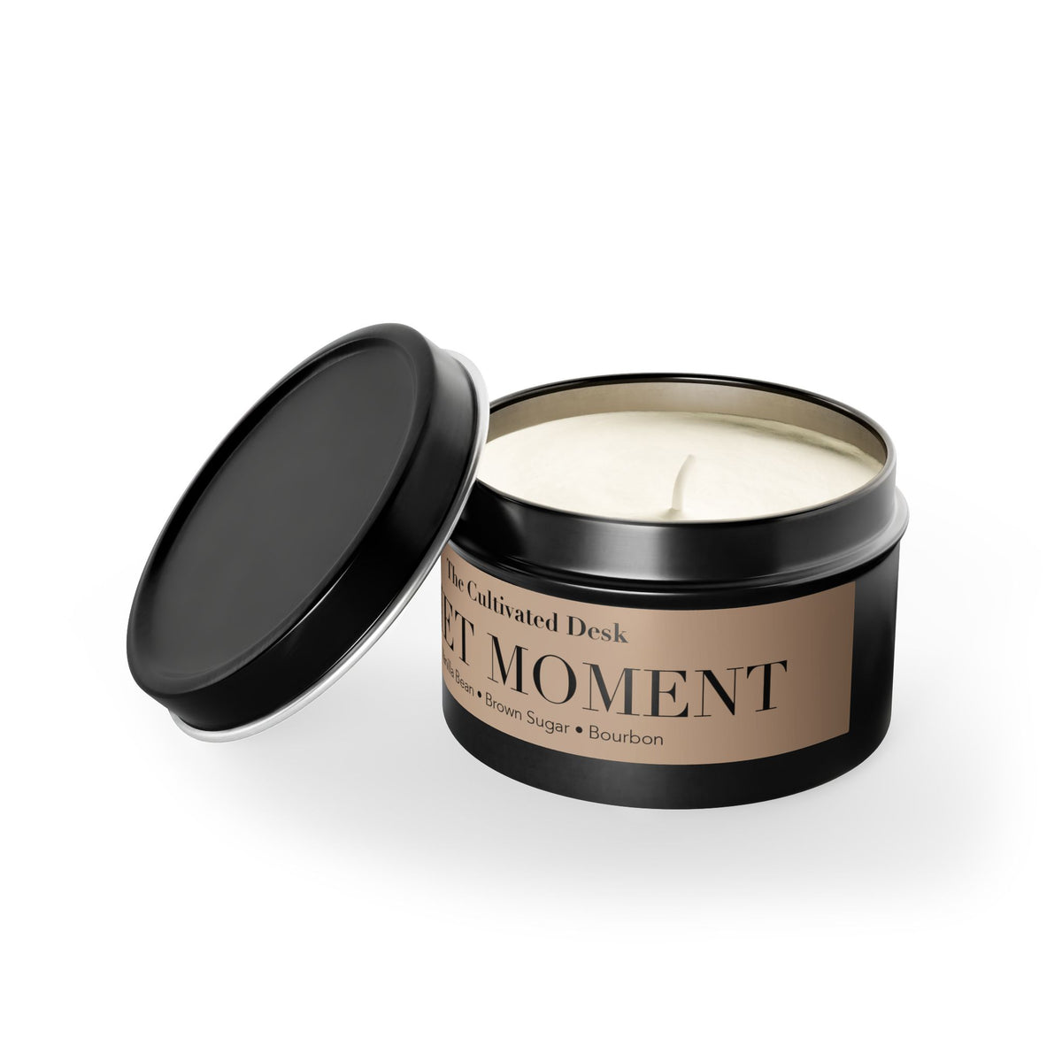 An open black metal candle tin with cream-colored soy wax, shown on a white background with its lid leaning against the container. The front label is tan and reads 'The Cultivated Desk' and 'QUIET MOMENT'.