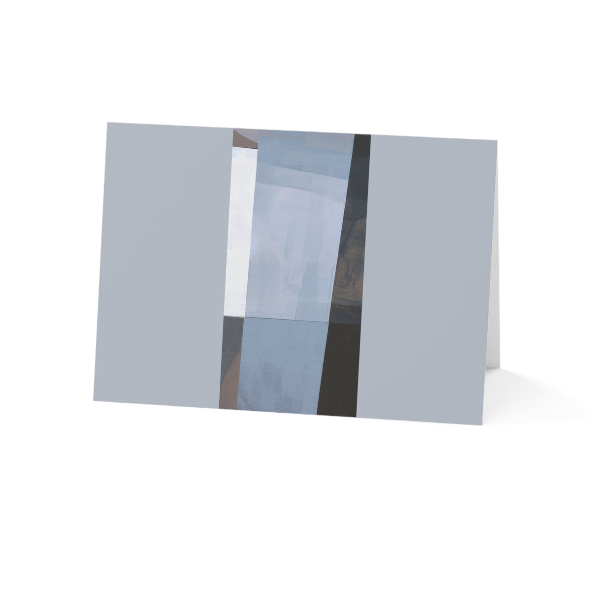 A folded greeting card standing upright on a white background, featuring an abstract geometric design with muted gray, light blue, white, and dark charcoal blocks.