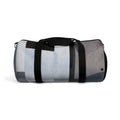 A cylindrical duffel bag with a modern abstract geometric pattern in shades of gray, blue, white, and black, featuring black webbing handles and a shoulder strap with silver metal hardware, shown against a plain white background.