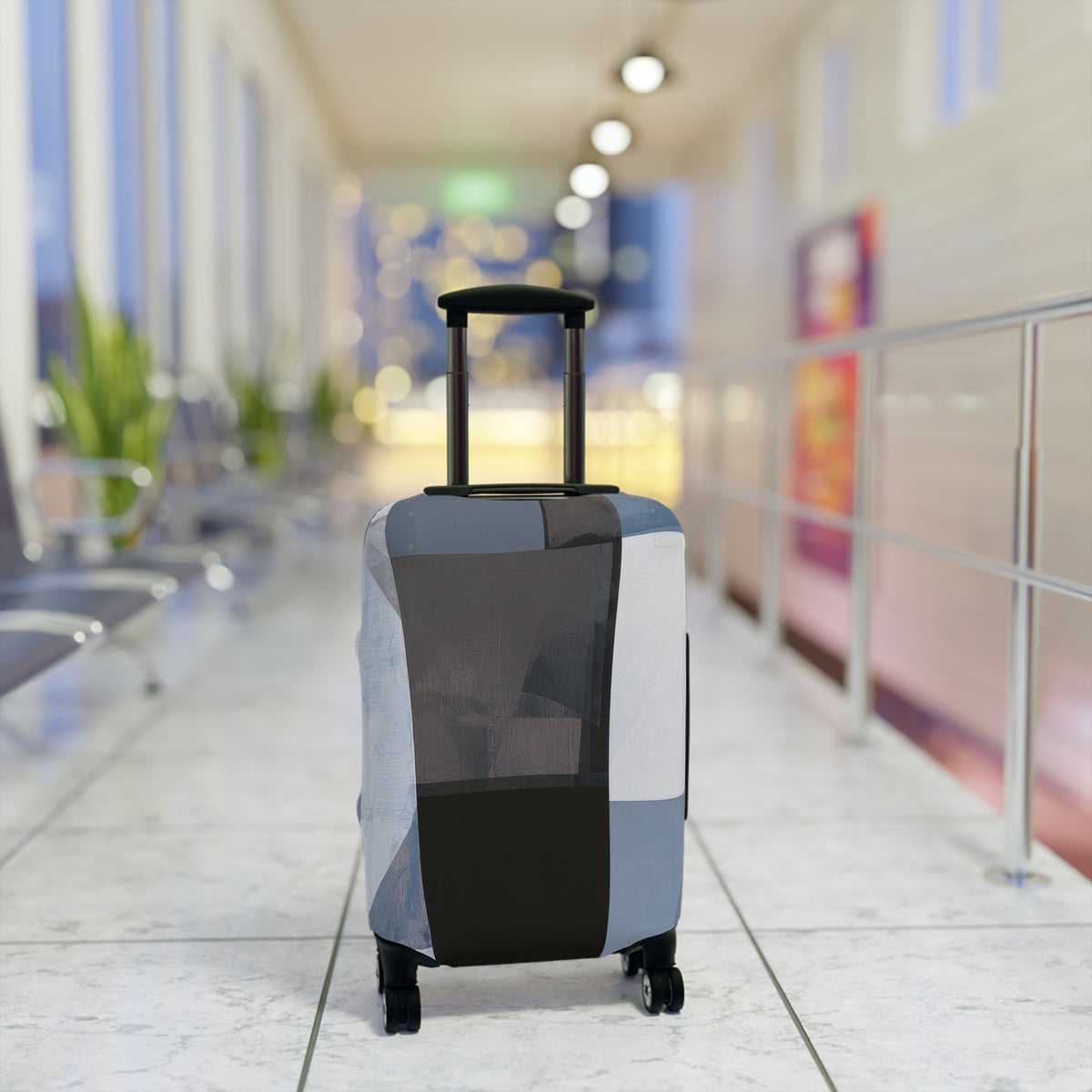 A hard-shell rolling suitcase with an extendable handle and four wheels, covered in a geometric patchwork luggage sleeve in shades of gray, black, and white. The suitcase is positioned in the center of a brightly lit, modern airport terminal corridor with a blurred background.