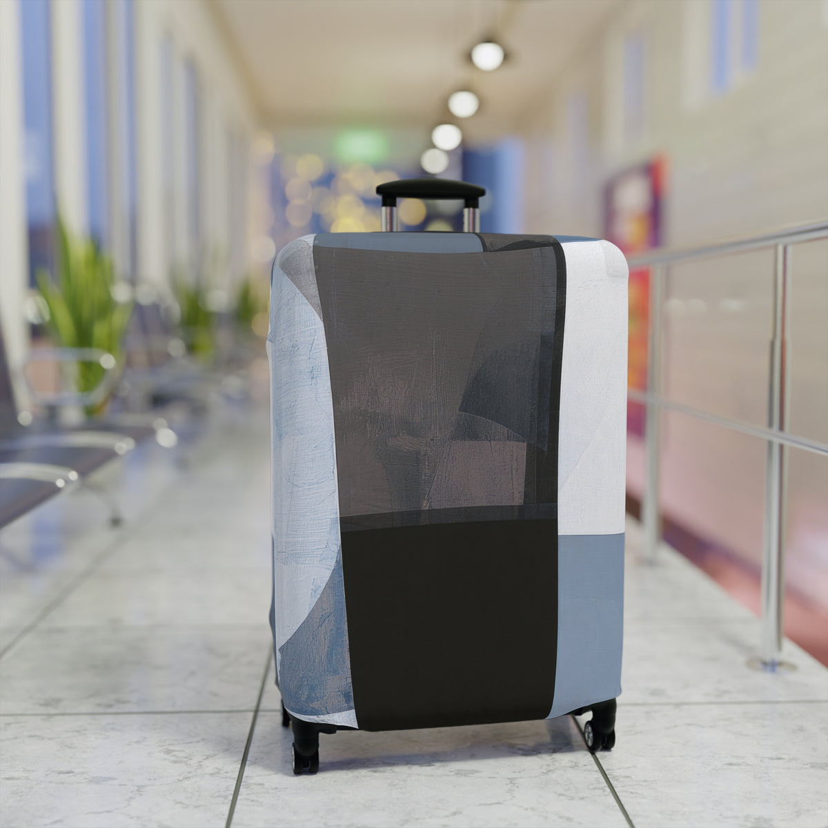 A rolling suitcase covered in a geometric patterned luggage sleeve, positioned in a brightly lit airport terminal corridor.