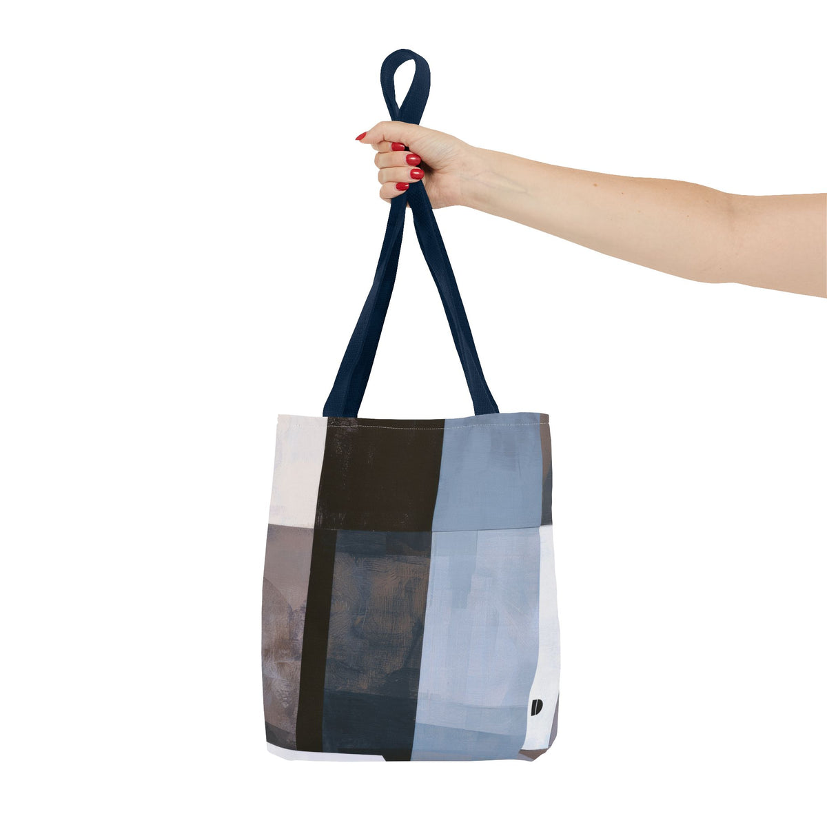 A woman is holding a large canvas tote bag with a geometric patchwork pattern in shades of blue, black, and gray. The photo is shot against a solid white background.