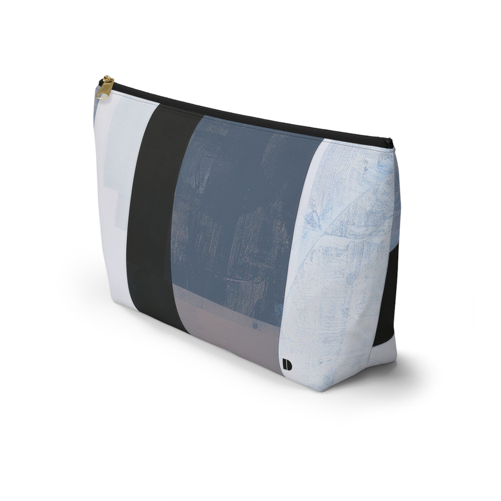 A rectangular zippered pouch with an abstract geometric patchwork pattern in shades of blue, gray, white, and charcoal, featuring a gold zipper pull and a small black logo on the bottom right.