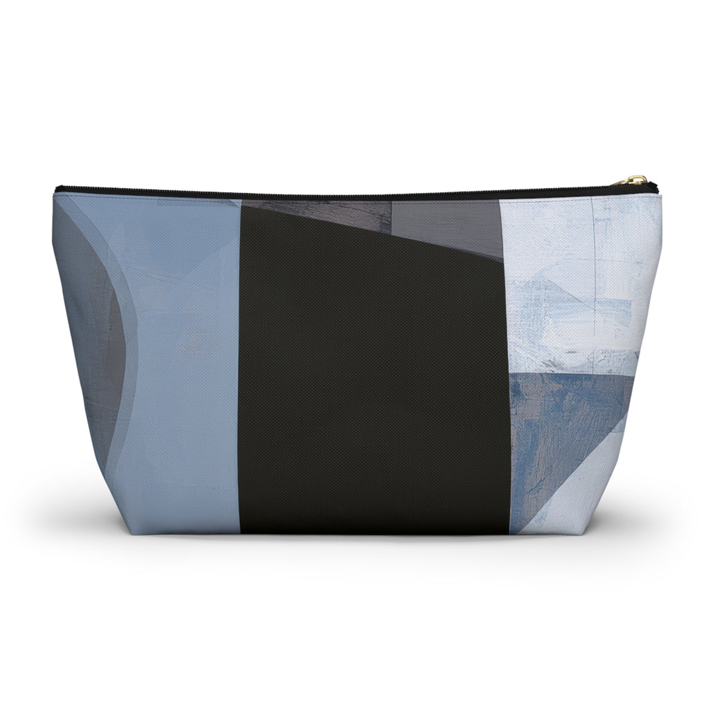 A rectangular zippered pouch with an abstract geometric patchwork pattern in shades of blue, gray, white, and charcoal, featuring a gold zipper pull.