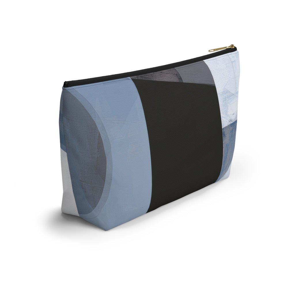 A rectangular zippered pouch with an abstract geometric patchwork pattern in shades of blue, gray, white, and charcoal, featuring a gold zipper pull.