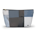 A rectangular zippered pouch with an abstract geometric patchwork pattern in shades of blue, gray, white, and charcoal, featuring a gold zipper pull and a small black logo on the bottom right.