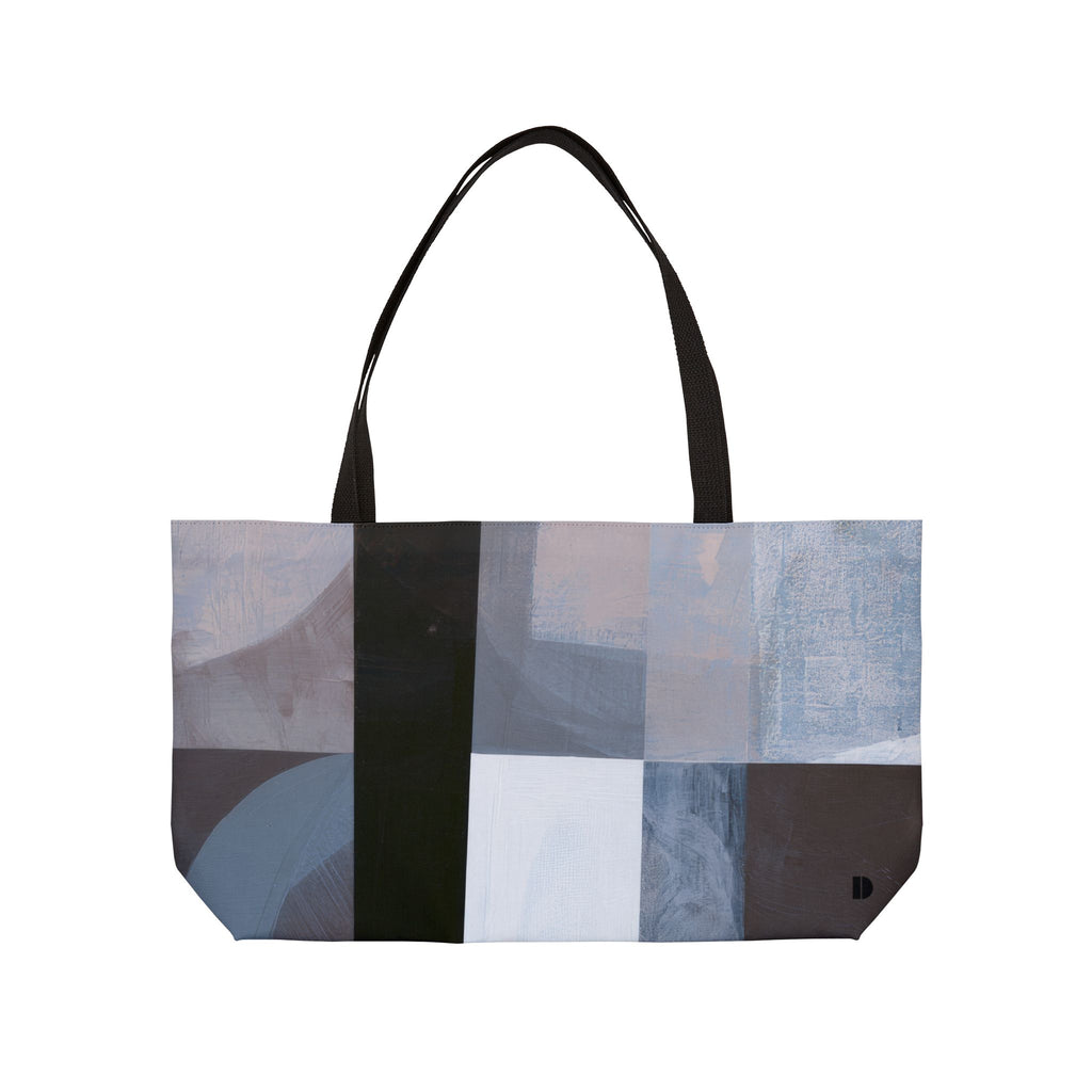A tote bag with a modern abstract geometric print in shades of gray, blue, beige, and black, featuring two black shoulder straps, shown against a plain white background.
