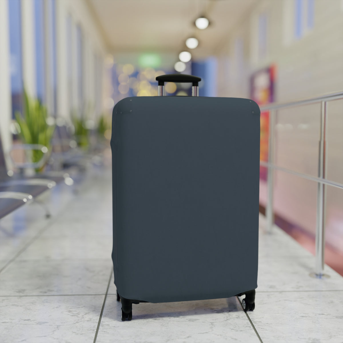 A dark slate blue or gray protective suitcase cover fitted on a rolling suitcase, standing in a blurred airport terminal hallway.