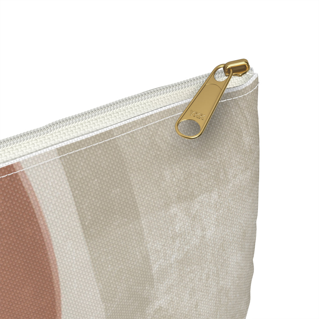 Close-up of a zippered pouch with a textured beige, rose, and white geometric pattern and a gold-tone metal zipper pull on a white background.