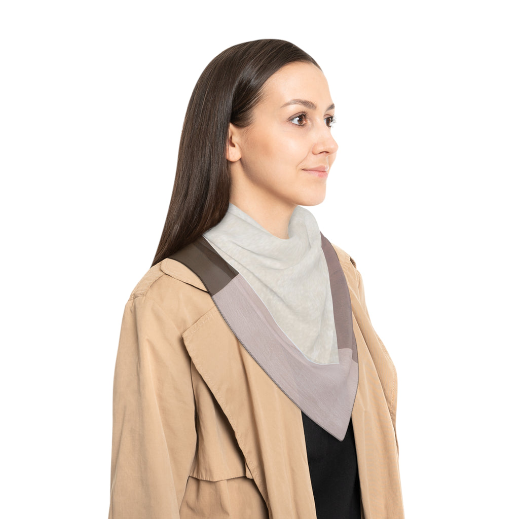 A woman in profile wearing a beige trench coat over a black top, with a light gray mock neck and a large draped scarf in taupe and brown.