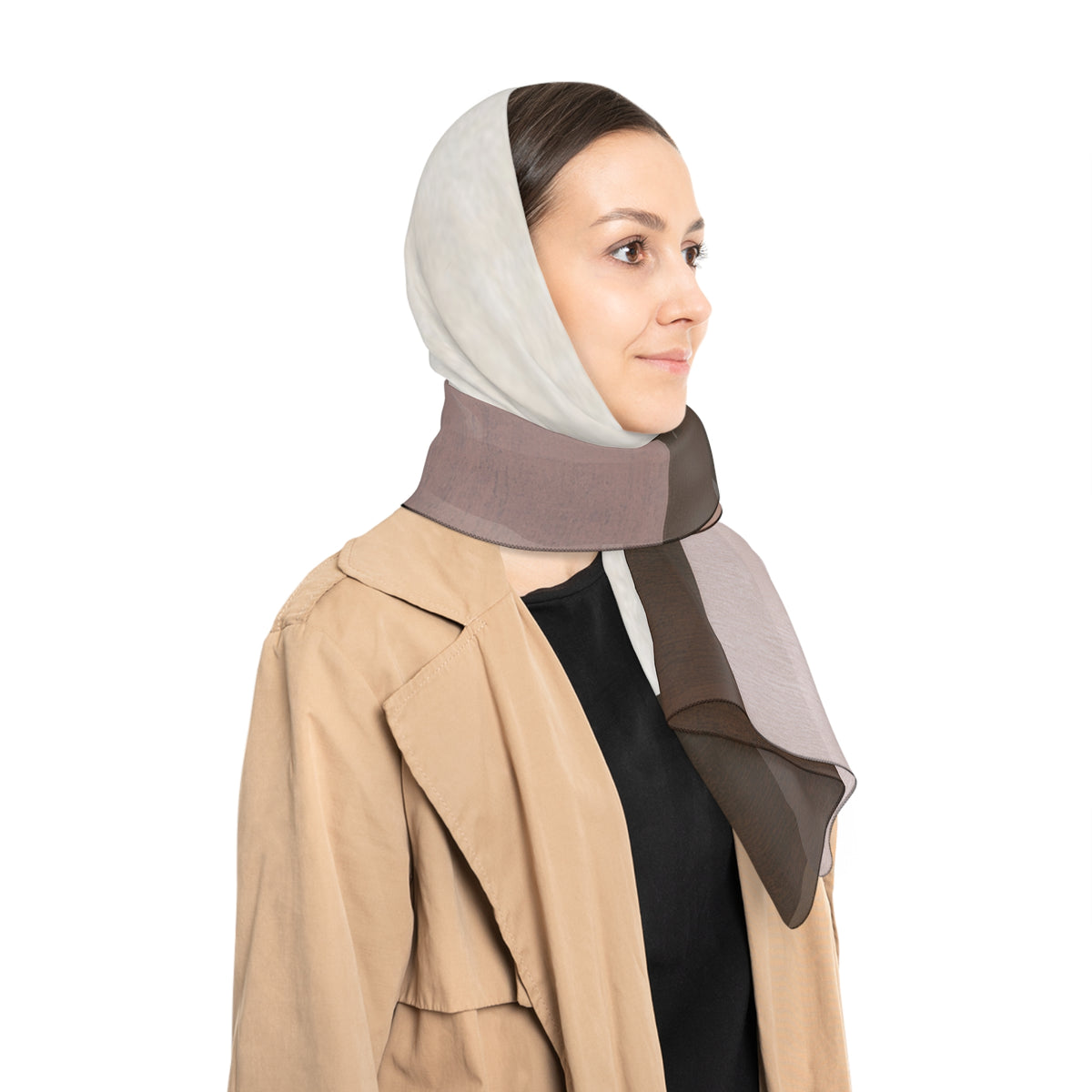 A woman wearing a beige trench coat over a black top, with a color-blocked scarf as a head scarf in light gray, taupe, and brown draped over her shoulder, against a solid white background.