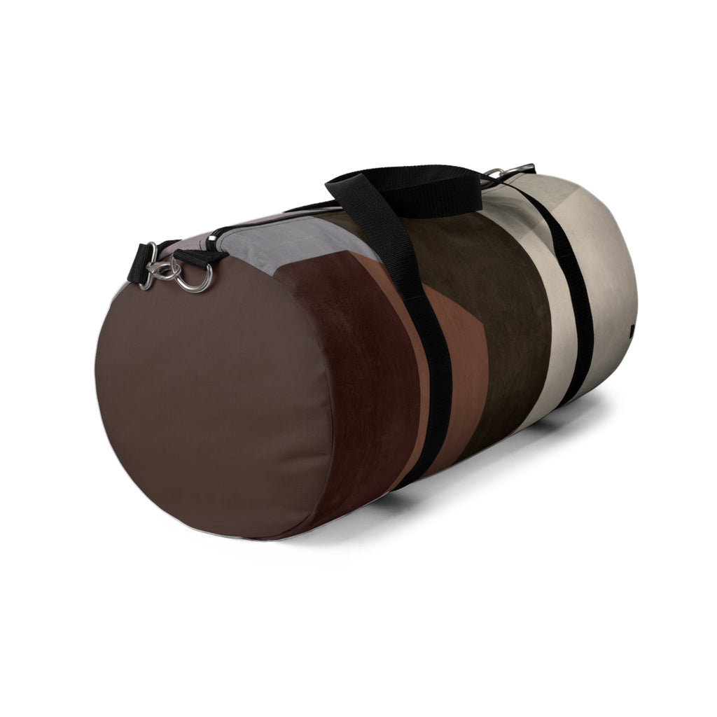A cylindrical duffel bag with a geometric color-blocked pattern in shades of brown, beige, and gray, featuring black straps and a silver metal D-ring, shown on a white background.