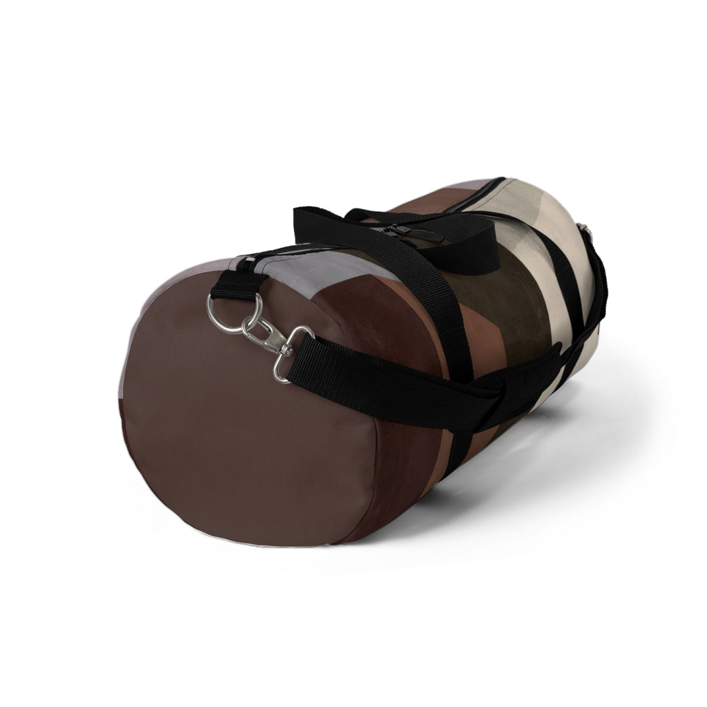 A cylindrical duffel bag with a geometric color-blocked pattern in shades of brown, beige, and gray, featuring black straps and a silver metal D-ring, shown on a white background.
