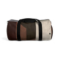 A cylindrical duffle bag with a geometric color-blocked pattern in shades of brown, beige, and gray, featuring black webbing handles and a shoulder strap with silver metal hardware, shown against a plain white background.