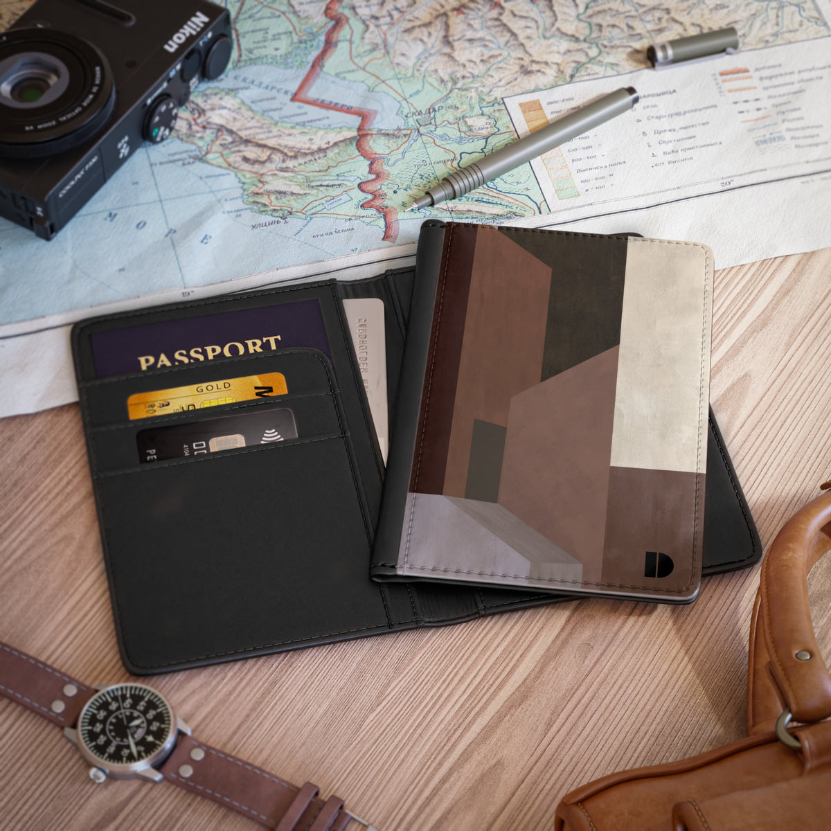 A faux leather passport holder and card case organizer shown open on a wooden surface, with a passport, cards, a map, camera, pen, watch, and leather bag around it.