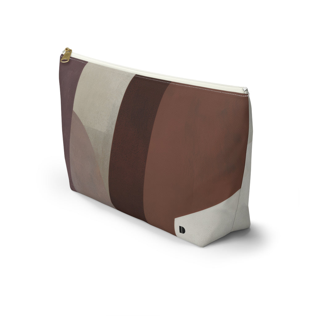 A rectangular zippered pouch with an abstract geometric color-block pattern in shades of brown, beige, and cream, featuring a gold zipper pull and a small black logo tab on the bottom right corner.