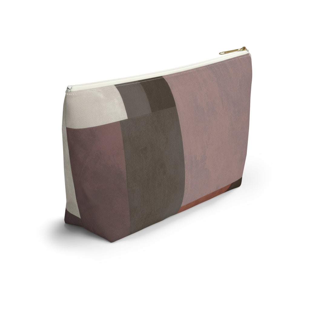 A rectangular zippered pouch with an abstract geometric patchwork pattern in muted tones of dusty pink, taupe, brown, and cream, featuring a gold zipper pull, shown on a white background.