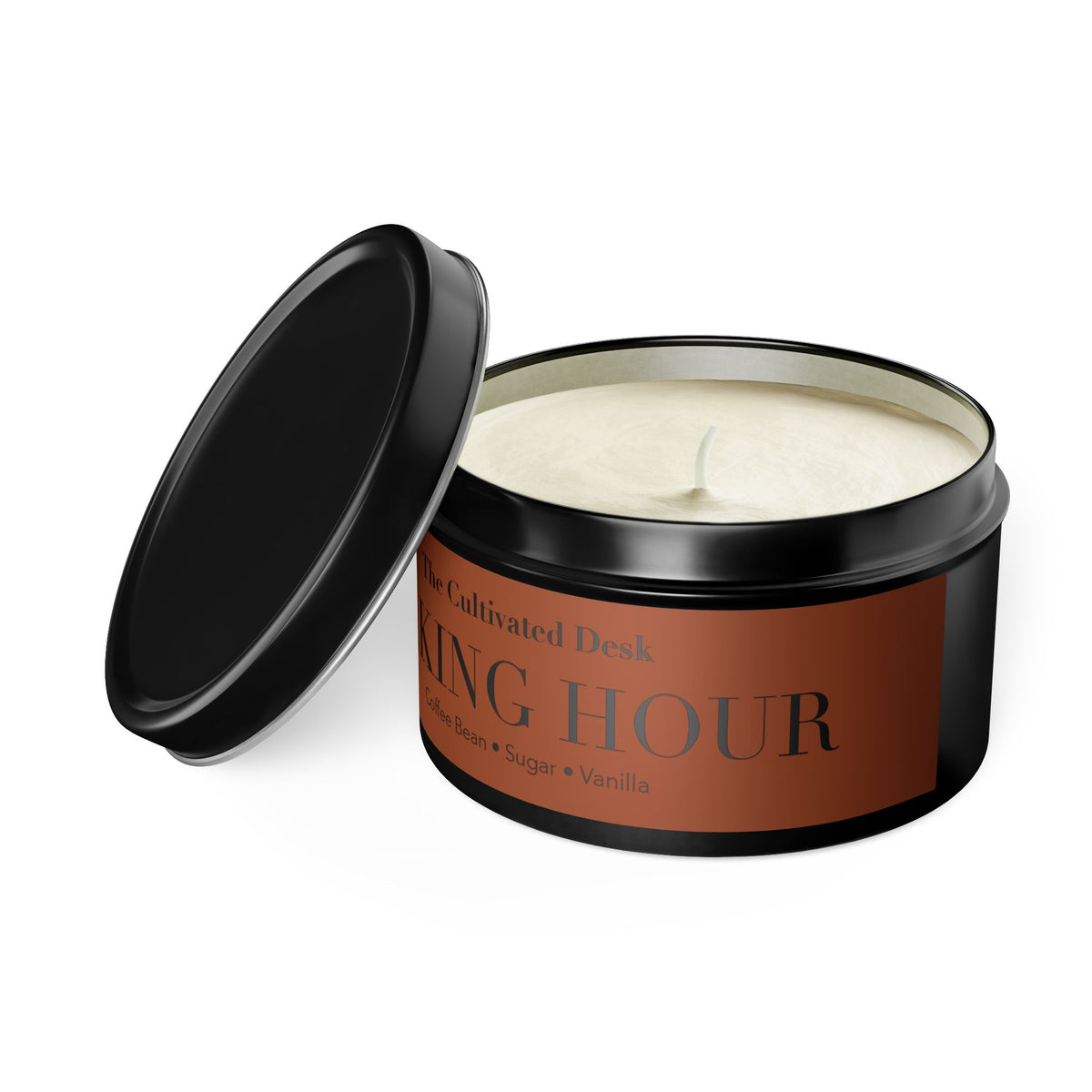 A  candle in a black metal tin with its lid leaning against the container. The soy candle wax is off-white, and the label is a warm terracotta brown with dark gray text reading 'The Cultivated Desk' and 'WAKING HOUR'.