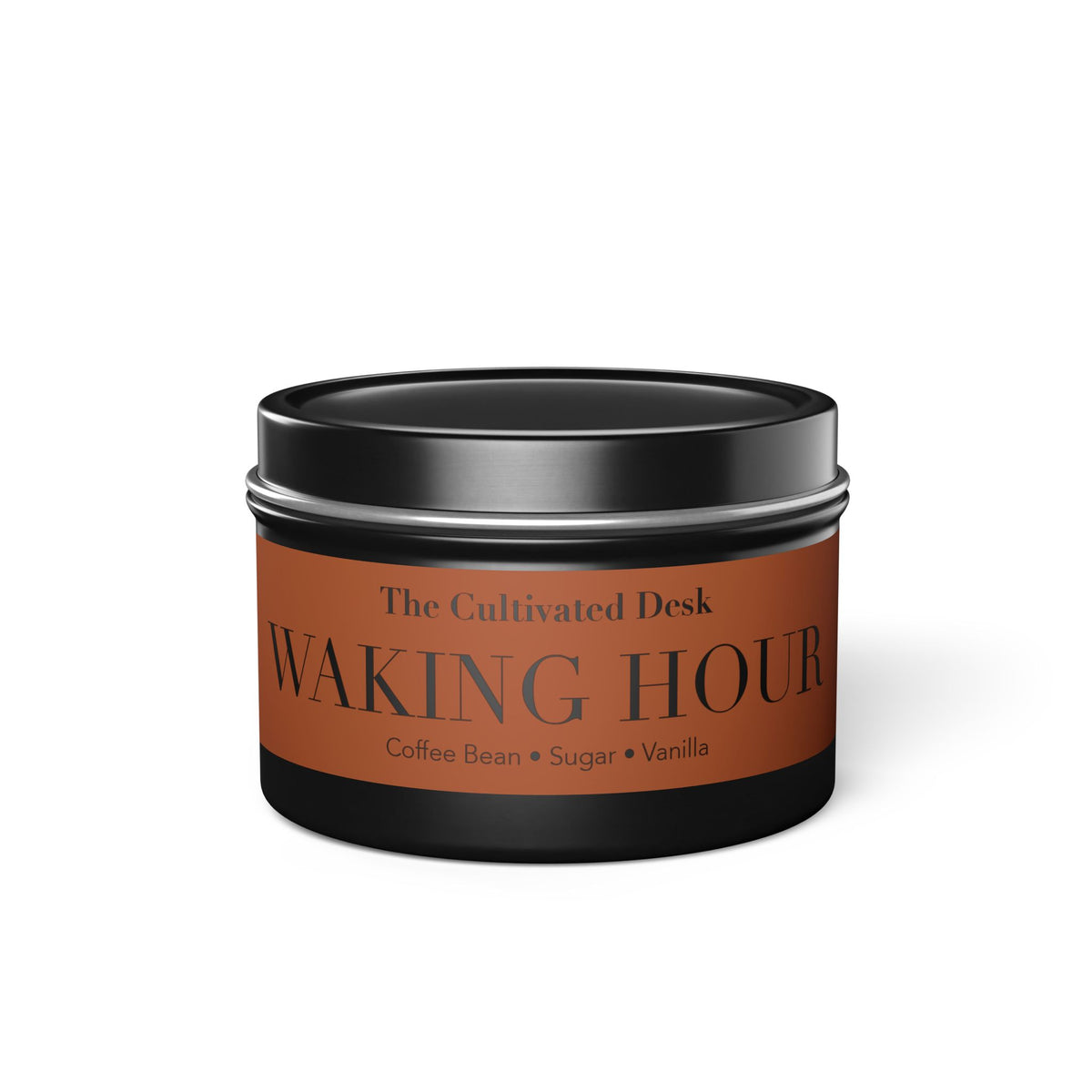 A round metal tin candle with a black lid and base, featuring a warm brown label that reads 'The Cultivated Desk WAKING HOUR' and 'Coffee Bean + Sugar + Vanilla' on a white background.
