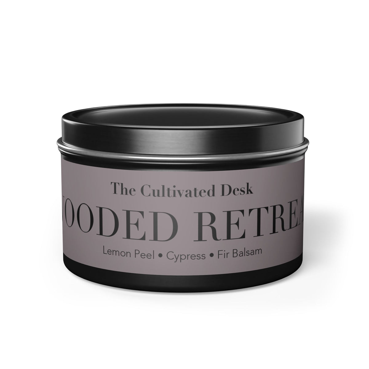 A round black metal tin candle jar with a muted taupe-gray label reading 'The Cultivated Desk' and 'WOODED RETIREAT' with scent notes 'Lemon Peel • Cypress • Fir Balsam' on a white background.